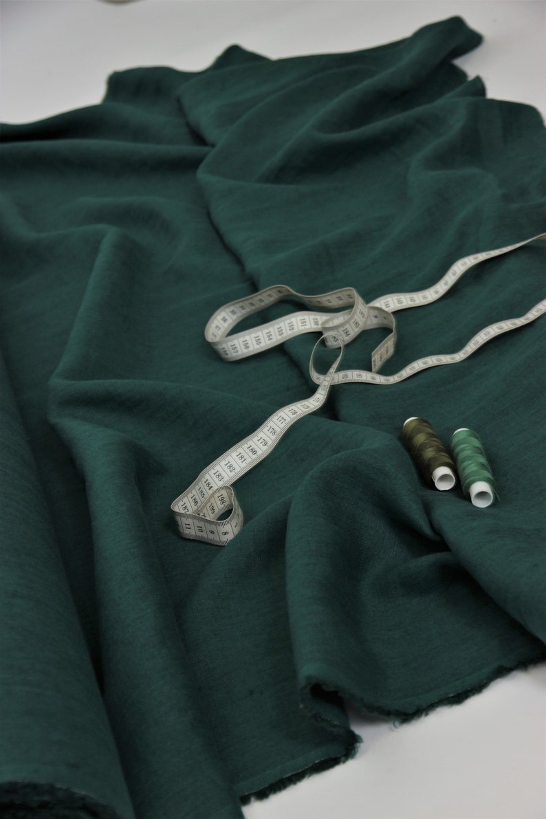 May include: A deep green fabric with a measuring tape and spools of thread. The fabric is folded and has a textured surface.