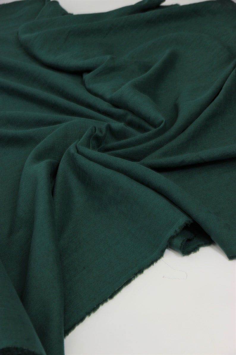 May include: A deep green fabric with a soft, textured surface. The fabric is folded and draped, showing its natural drape and texture.