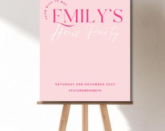 Puede incluir: Un letrero rectangular de color rosa claro con texto en rosa oscuro y blanco. El texto dice FROM MISS TO MRS, EMILY'S, Hens Party, SATURDAY 3RD DECEMBER 2022 y #FUTUREMRSSMITH. El letrero se exhibe sobre un caballete de madera de tres patas.