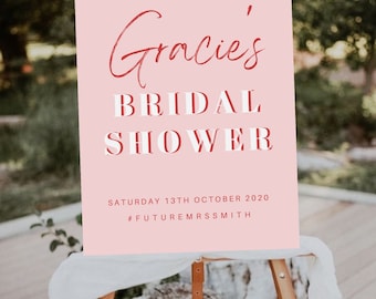 Puede incluir: Un letrero rectangular de color rosa con texto en blanco y rojo que dice WELCOME TO Gracie's BRIDAL SHOWER SATURDAY 13TH OCTOBER 2020 #FUTUREMRSSMITH. El letrero se exhibe en un caballete de madera, con una fuente cursiva y letras de bloque.