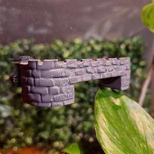 Op de afbeelding: Een grijze 3D-geprinte stenen brug voor een reptielen terrarium. De brug is ontworpen om eruit te zien als een middeleeuwse kasteelmuur met een getextureerd oppervlak.