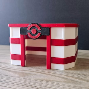 Pode incluir: Um edifício listrado de vermelho e branco com um logotipo circular preto e vermelho acima da entrada. O edifício tem um telhado plano e uma pequena porta.