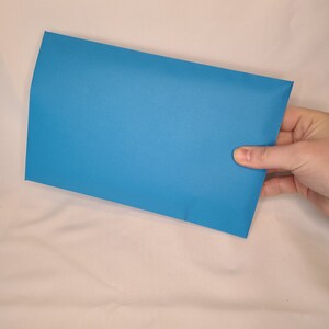 May include: A bright blue envelope, held in a hand, against a white background.