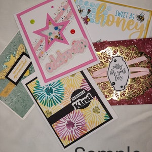 May include: A collection of handmade greeting cards with various designs and messages. The cards feature a pink card with a star and the word "celebrate", a green card with a floral pattern and the words "You are much appreciated", a yellow card with a floral pattern and the words "You have been so Kind", a honey-themed card with the words "Sweet as honey", and a burgundy card with a gold frame and the words "sorry for your loss".