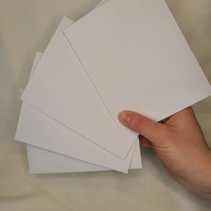May include: A stack of five white blank cards, held in a hand.