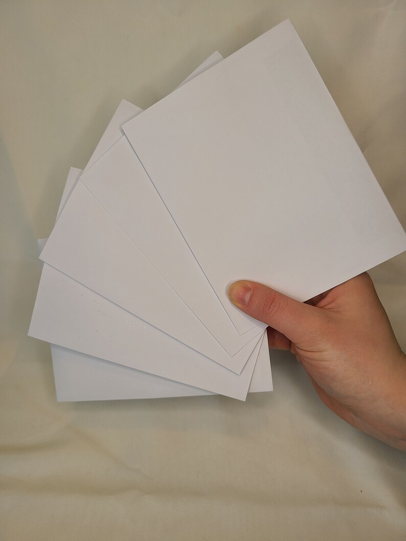 May include: A stack of five white blank cards, held in a hand.