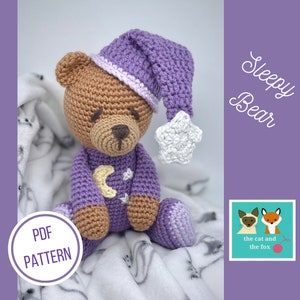 May include: A crocheted purple and brown sleepy bear wearing a purple sleeping cap with a white star. The bear is sitting on a white blanket with a gray pattern. The text "Sleepy Bear" is in the upper right corner of the image. The text "PDF PATTERN" is in the lower left corner of the image.
