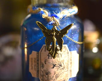 Könnte beinhalten: Eine blaue Glasflasche mit goldenem Deckel und einem Feen-Anhänger. Die Flasche hat ein Etikett mit der Aufschrift "Fairy Honey".