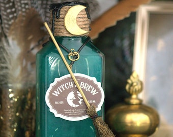 Może przedstawiać: Zielona szklana butelka z etykietą „Witch Brew” i złotym półksiężycem na górze. Butelka jest ozdobiona sznurkiem i czarnym sznurkiem ze złotym wisiorkiem. Mały miotła jest przymocowany do butelki.