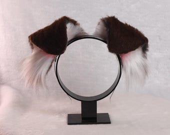 May include: Brown and white furry cat ears headband on a black stand. The headband is made of soft, plush fabric and has a wire inside to help it keep its shape.