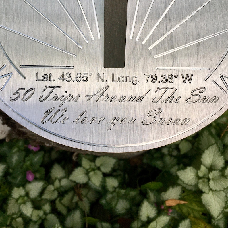 May include: A silver metal plaque with the text "Lat. 43.65&deg; N, Long. 79.38&deg; W 50 Trips Around The Sun We love you Susan" engraved on it.