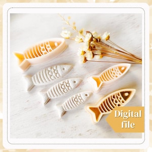 以下が含まれることがあります： さまざまなサイズの白いプラスチック製の魚の形をしたクッキーカッターが5つ。カッターはテクスチャ加工が施されており、白い表面に配置されています。デジタルファイルです。