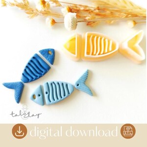 以下が含まれることがあります： 青と黄色の3つの魚の形をしたオブジェクトが白い表面に配置されています。魚には、詳細なひれと体のデザインがあります。画像には「digital download」というテキストが含まれています。