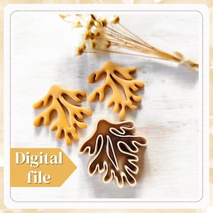 Op de afbeelding: Drie bruine plastic koekjesvormen in de vorm van zeewier of koraal. De vormen liggen op een wit oppervlak met een boeket gedroogde bloemen op de achtergrond. De tekst "Digitaal bestand" staat in geel op een witte achtergrond.