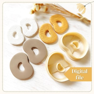 Op de afbeelding: Een set van drie koekjesvormen in de vorm van een bagel met hartvorm. De vormen zijn gemaakt van helder plastic en worden getoond op een wit houten oppervlak. De vormen worden geleverd met drie voorbeelden van de koekjesvorm gemaakt in witte, bruine en gele polymer klei.
