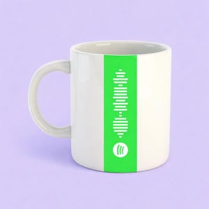 May include: White ceramic mug with a green vertical stripe and a white Spotify code design. The mug has a white handle. The Spotify logo is at the bottom of the green stripe. The background is a light purple colour.