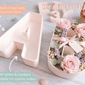 Puede incluir: Una letra decorativa "B" llena de rosas rosas, lavanda y vegetación, atada con una cinta rosa y una etiqueta. Al lado hay una letra "A" vacía. El texto de la imagen dice "DECORATIVE BOX" y "Disponible en dos tamaños: 30 cm y 20 cm".