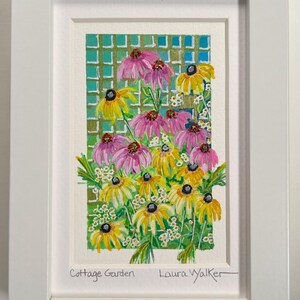 May include: A framed watercolor painting of a cottage garden scene. The artwork features vibrant pink and yellow coneflowers and black-eyed Susans against a green trellis. The painting is signed "Laura Walker" and titled "Cottage Garden".