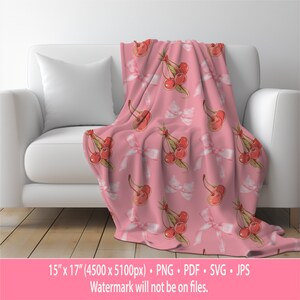 May include: Pink throw blanket with a repeating pattern of red cherries and white bows. The blanket is 15 inches by 17 inches.