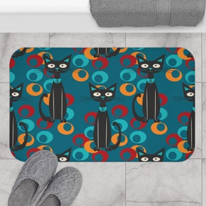 May include: A teal blue bath mat with a repeating pattern of black cats and colourful circles. The cats are sitting with their tails curled around their legs. The circles are in shades of orange, red, and blue.