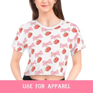 May include: White crop top with a pink and white cherry print. The cherries have pink bows.