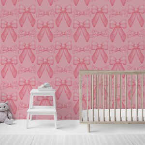 May include: Pink and white gingham bow pattern wallpaper with a white crib in the foreground.