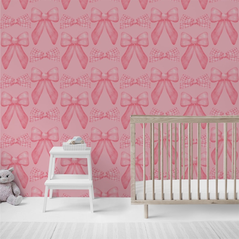 May include: Pink and white gingham bow pattern wallpaper with a white crib in the foreground.