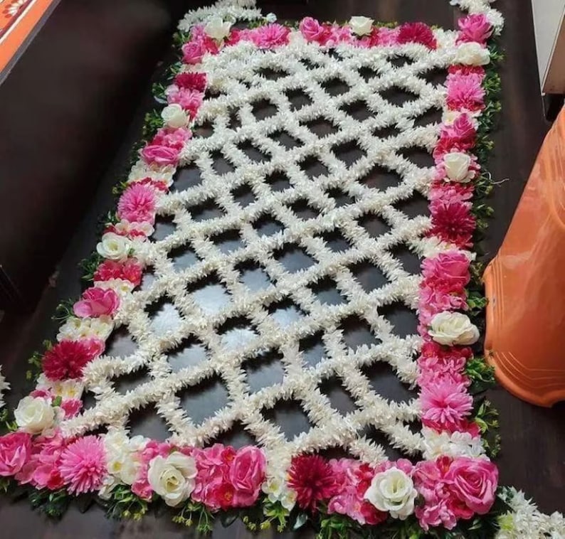 May include: A white floral design with a diamond pattern, surrounded by a border of pink and white flowers.