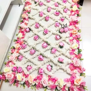 May include: A white and pink floral arrangement with a diamond pattern in the center. The arrangement is made of white flowers and pink roses. The text "Ud" is visible in the center of the arrangement.