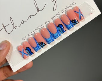 May include: A set of ten press-on nails with a light pink base and blue butterfly designs. The nails are arranged in a row on a white card with the text "Thank you for supporting my small business".