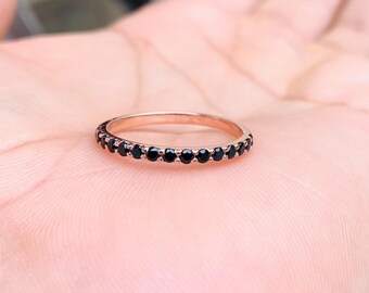 May include: A thin rose gold band ring featuring a continuous row of small, round, faceted black stones set in a prong setting that encircles the entire circumference of the metal band, creating a delicate and uniform circular jewellery piece.