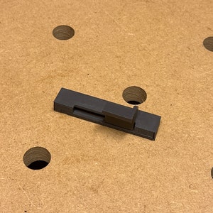 Puede incluir: Un jig de madera de plástico negro con un mecanismo deslizante. El jig está diseñado para ayudar con los proyectos de carpintería.