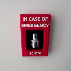 May include: Red plastic box with the text "IN CASE OF EMERGENCY" and a 10 mm socket inside. The box is mounted on a white wall.