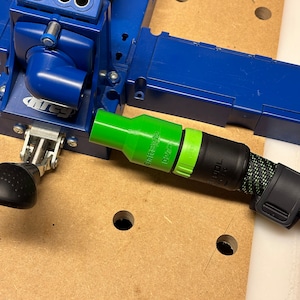 May include: A green and black drill bit attachment with the text "Craft Style D2721" and "DEWALT" on it. The attachment is connected to a blue and black drill press.