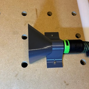 Könnte beinhalten: Ein grauer 3D-gedruckter Staubauffangtrichter, der mit Schrauben an einer Wand befestigt ist. Der Trichter ist mit einem schwarzen und grünen Schlauch mit einer schwarzen und grünen Schlauchschelle verbunden.