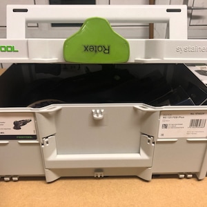 Puede incluir: Una caja de herramientas Festool Systainer 3 gris y verde con una lijadora Rotex RO 125 FEG-Plus negra y verde en su interior. La caja tiene una manija verde con la palabra "Rotex" impresa en ella. La caja tiene una etiqueta en el lateral que dice "No. 374029" y "RO 125 FEG-Plus".