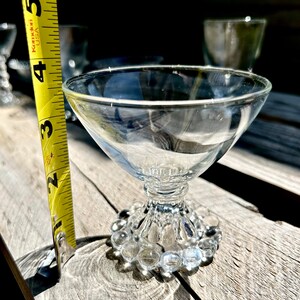 K&ouml;nnte beinhalten: Eine klare Glasschale mit Stiel und einer perlenbesetzten Basis. Die Schale steht auf einer Holzoberfl&auml;che.