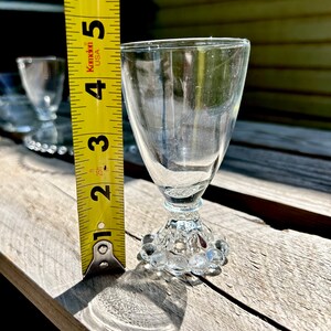 K&ouml;nnte beinhalten: Ein Satz von vier klaren Schnapsgl&auml;sern aus Glas mit einem perlenbesetzten Fu&szlig;. Die Gl&auml;ser sind etwa 7,6 cm hoch. Ein gelbes Ma&szlig;band befindet sich im Hintergrund.