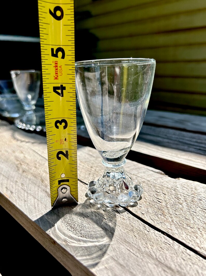 K&ouml;nnte beinhalten: Ein Satz von vier klaren Schnapsgl&auml;sern aus Glas mit einem perlenbesetzten Fu&szlig;. Die Gl&auml;ser sind etwa 7,6 cm hoch. Ein gelbes Ma&szlig;band befindet sich im Hintergrund.