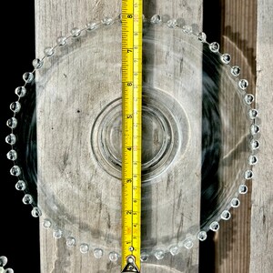 K&ouml;nnte beinhalten: Ein klarer Glaskuchenst&auml;nder mit einem perlenbesetzten Rand. Der St&auml;nder hat einen Durchmesser von 20 cm und steht auf einer Holzoberfl&auml;che.