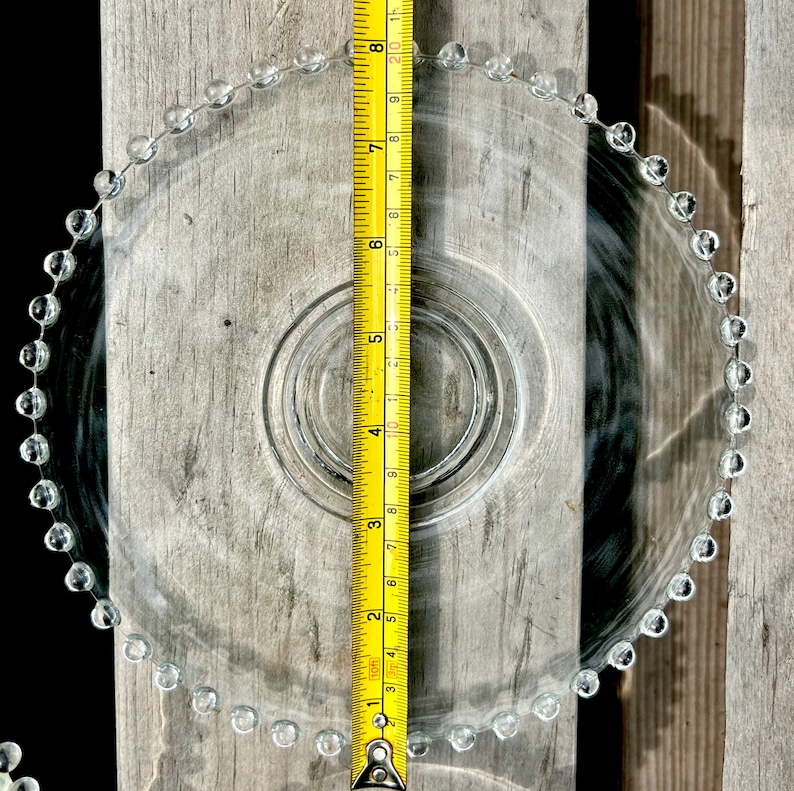 K&ouml;nnte beinhalten: Ein klarer Glaskuchenst&auml;nder mit einem perlenbesetzten Rand. Der St&auml;nder hat einen Durchmesser von 20 cm und steht auf einer Holzoberfl&auml;che.