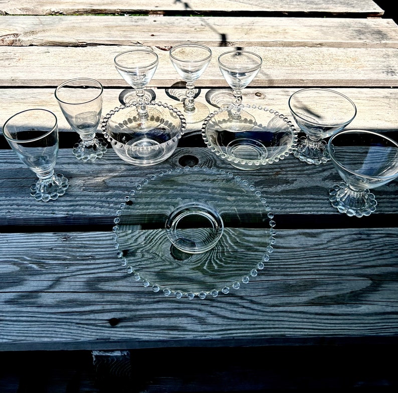 K&ouml;nnte beinhalten: Ein Set aus klaren Glasschalen mit Perlenrand. Die Schalen sind auf einer Holzoberfl&auml;che mit einer gr&ouml;&szlig;eren, perlenbesetzten Glasservierplatte in der Mitte angeordnet.