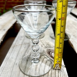 K&ouml;nnte beinhalten: Drei klare Schnapsgl&auml;ser aus Glas mit einem perlenbesetzten Stiel. Die Gl&auml;ser stehen auf einer Holzoberfl&auml;che mit einem gelben Ma&szlig;band.