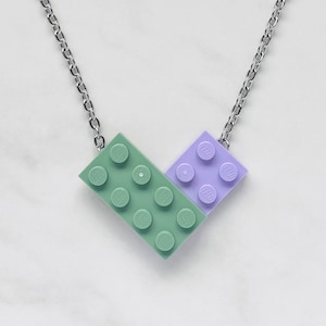 May include: A silver chain necklace with a green and purple LEGO brick pendant. The pendant is shaped like a heart.