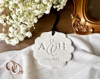 May include: White ceramic ornament with a scalloped edge, featuring the initials "A & H" and the text "EST. 2023".