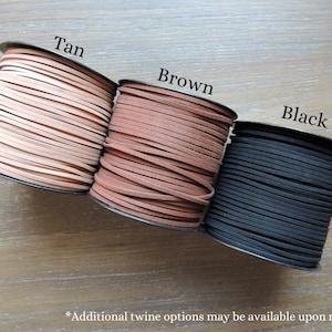May include: Three spools of leather cord in tan, brown, and black. The spools are labeled with the colors.