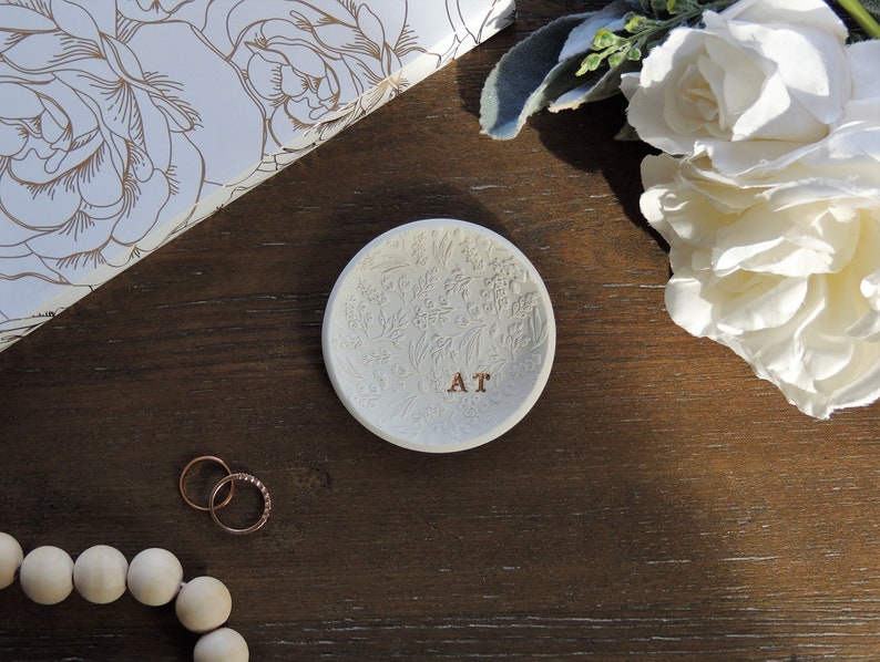 May include: White ceramic ring dish with a floral design and the initials "AT" in gold lettering.