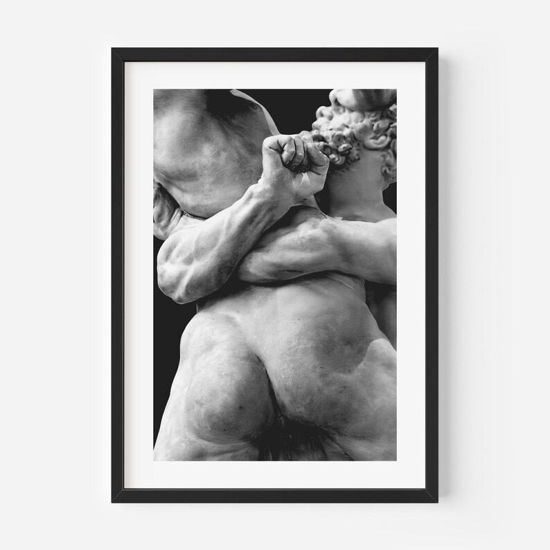 May include: Black and white framed print of a classical sculpture depicting two figures in a dynamic embrace. The sculpture is detailed, showing muscular forms and intricate textures. The artwork is set against a dark background.