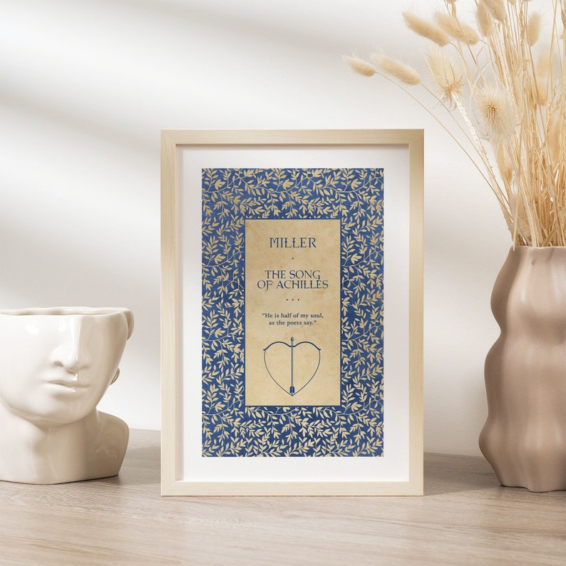 May include: A framed print of a book cover with a blue background and gold leaf design. The title of the book is "The Song of Achilles" by Madeline Miller. The quote "He is half of my soul, as the poets say" is printed below the title.