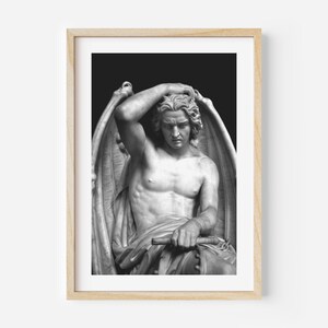 May include: Black and white photograph of a marble sculpture of a winged figure with a sorrowful expression. The figure is seated and has its head resting on its hand. The sculpture is set against a dark background.